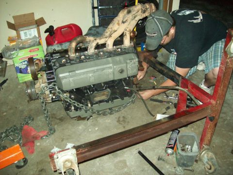 1985 Ford Bronco - A person works on an engine mounted on a red stand in a garage.