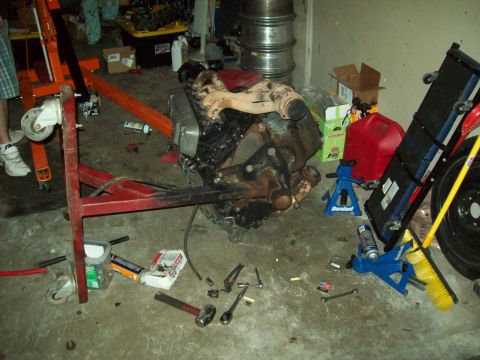 1985 Ford Bronco - Engine assembly being worked on in a garage setting with an engine stand and various tools.