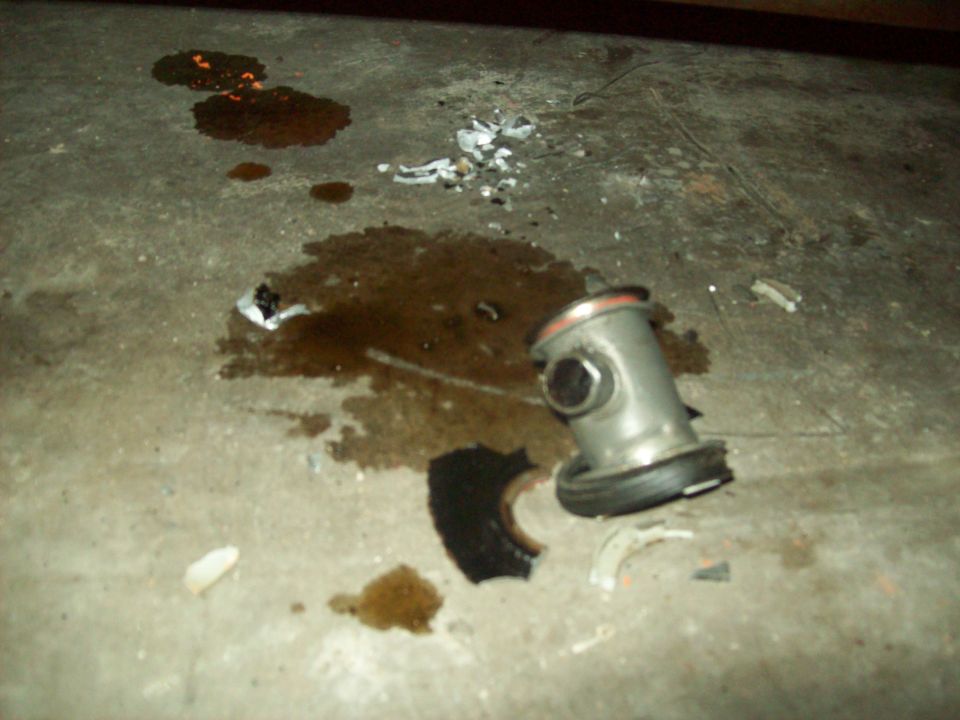 Broken metal part on concrete floor with fluid spills and debris