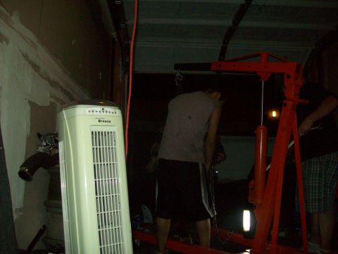 1985 Ford Bronco - People work in a garage with an engine hoist and a tall fan visible.