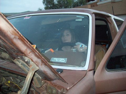 1985 Ford Bronco - A woman sits behind the wheel of a brown SUV with its hood open, revealing engine parts.