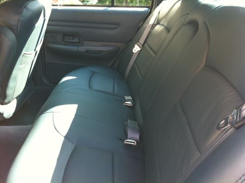 1999 Ford Crown Victoria - The rear interior of a car shows dark leather seats and seatbelts, with a watermark for Supermotors.net.