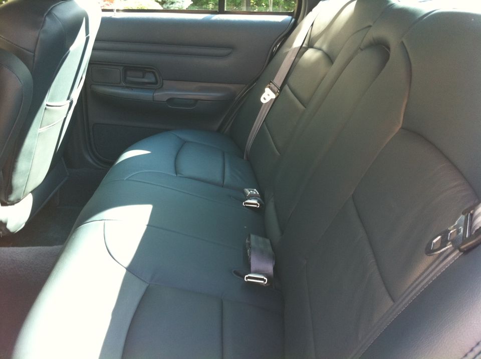 Back seat of a car with dark leather upholstery and seatbelts
