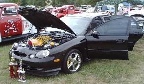 1997 Ford Taurus - A black 1997 Ford Taurus is shown with its hood and doors open, accompanied by several trophies.