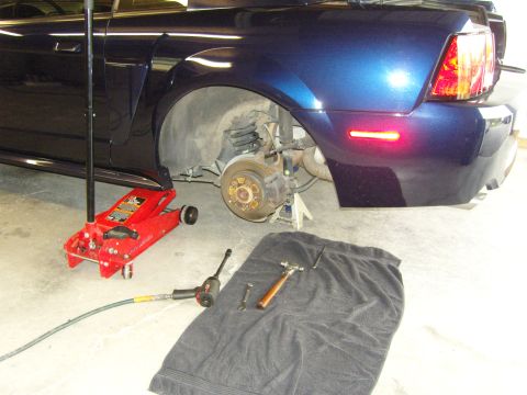 2007 Ford Mustang - The rear wheel assembly of a dark blue car is exposed, with tools laid out for maintenance.