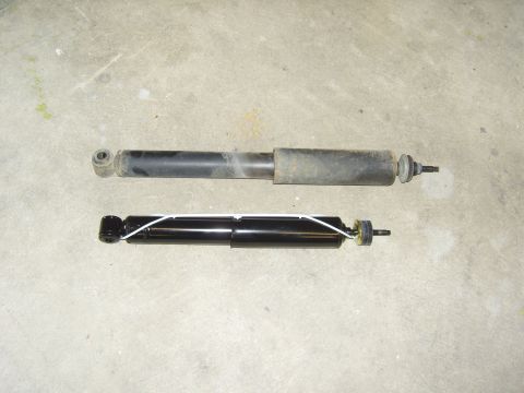 2007 Ford Mustang - Comparison of a used shock absorber with a new one, laid out on a concrete surface.