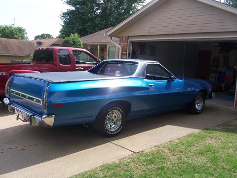 1973 Ford Ranchero - A blue Ford Ranchero is parked in front of a garage, with a red pickup truck beside it.
