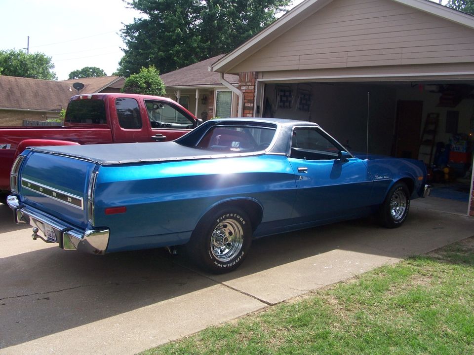 Blue 1972 Ford Ranchero with a black tonneau cover parked in a driveway next to a red pickup truck