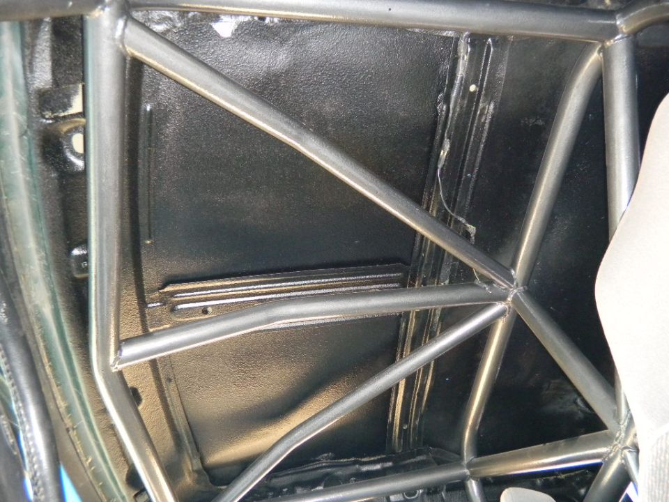 Roll cage inside a vehicle's interior, with black textured flooring and a partial view of a white seat