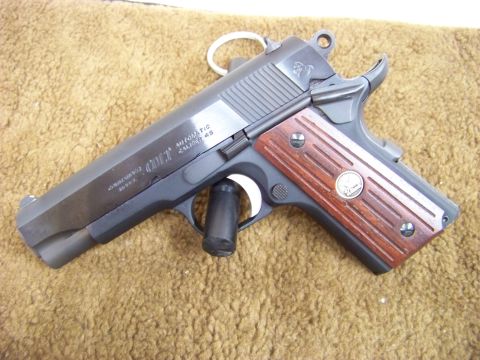 1995 Mercury Grand Marquis - A close-up view of a Colt 1911 pistol with wooden grip panels.