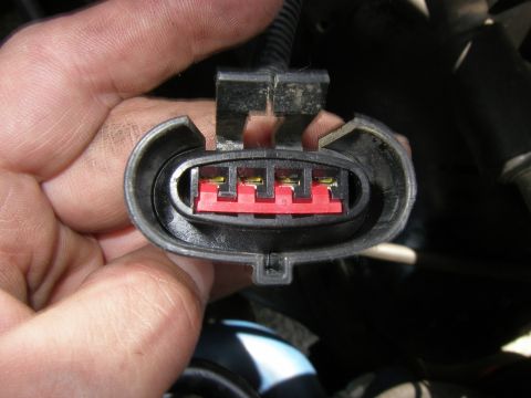 1990 Ford Bronco - A hand holds a four-pin electrical connector, showing the metal terminals within the red plastic housing.