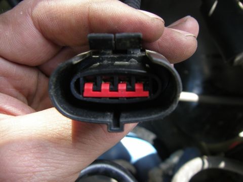 1990 Ford Bronco - A hand holds a black electrical connector with a red insert, showing four pins, likely for a vehicle's mass air sensor.