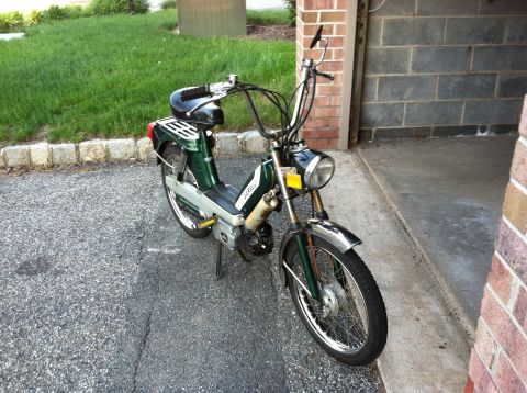 1981 Garelli Rally Sport - A green moped is parked on an asphalt surface next to a brick wall and garage.