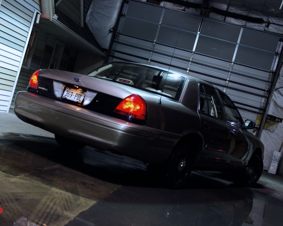 Rear view of tan Ford Crown Victoria sedan with black steelies at night by a garage door