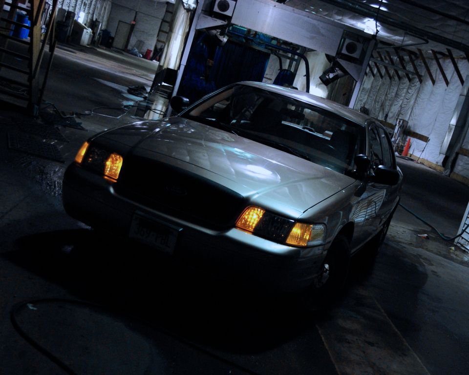 Silver Ford Crown Victoria sedan with amber parking lights on, parked inside a dark car wash bay