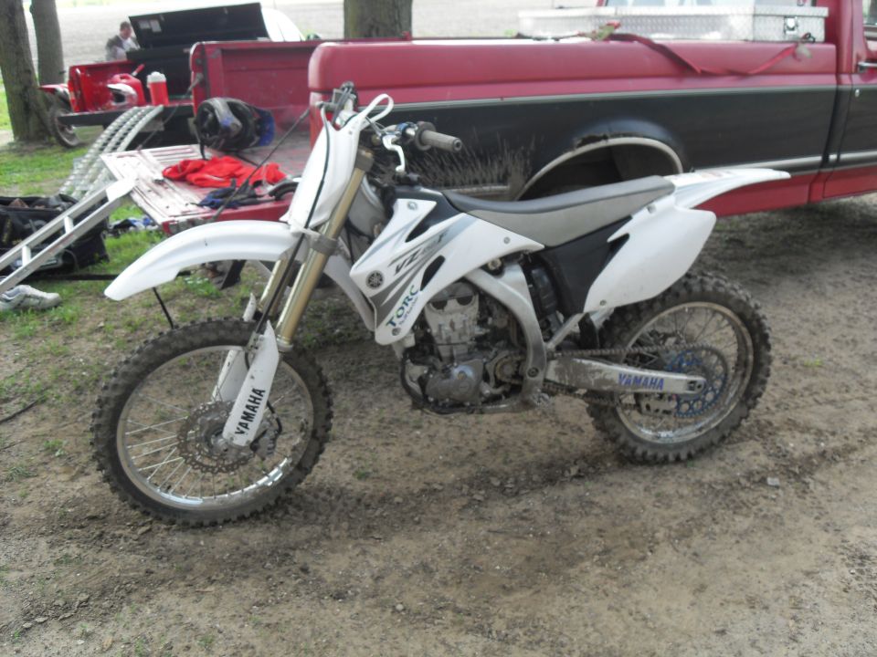 White Yamaha YZ450F dirt bike parked on dirt, with a red truck in the background