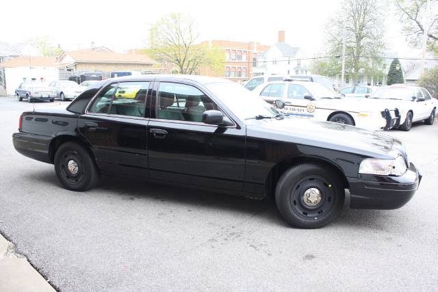 Black 2005 Ford Crown Victoria police car, 3/4 front view, parked with other police vehicles