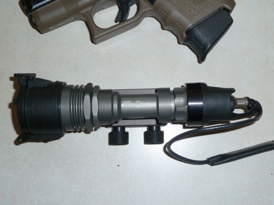 Tactical flashlight mounted on a rail, with a pistol grip and slide visible above