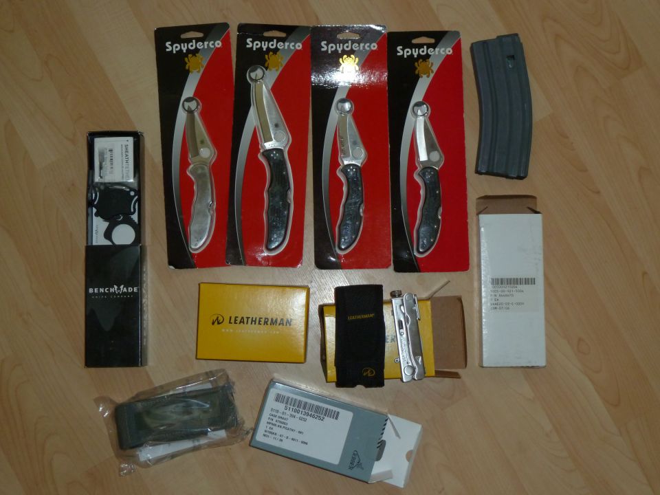 Several Spyderco knives, a Benchmade product, Leatherman tools, and a rifle magazine laid out on a wooden floor