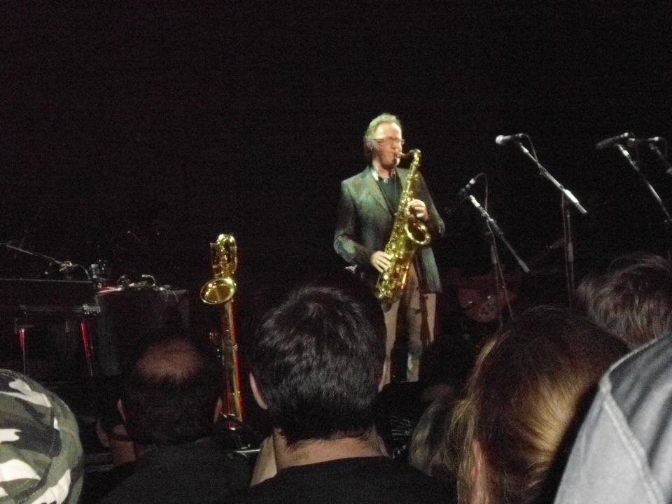 Man in a suit playing a saxophone on a dimly lit stage with microphones