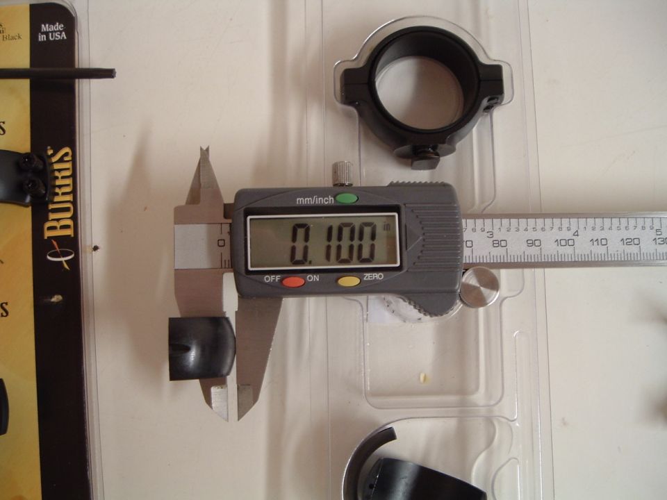 Digital caliper measuring a black cylindrical part to 0.100 inches. Packaging and ruler visible