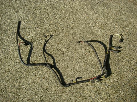 1990 Ford Bronco - A removed automotive wiring harness laid out on a sunlit concrete driveway, with black cloth tape and split-loom conduit covering the branc…