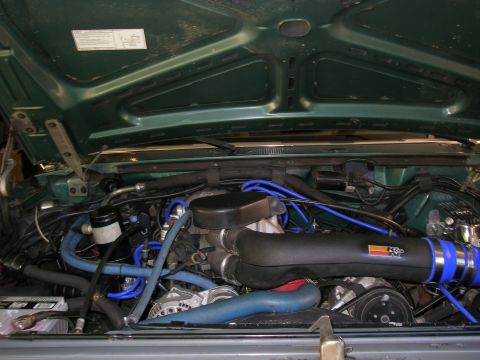 1990 Ford Bronco - Engine bay of a green Ford truck with the hood raised, showing a fuel-injected V8 fitted with a black K&N cold-air intake tube clamped with…