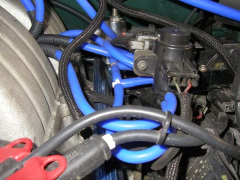 1990 Ford Bronco - Close-up of an engine bay showing bright blue aftermarket spark-plug wires routed across the intake, black braided looms and connectors, an…