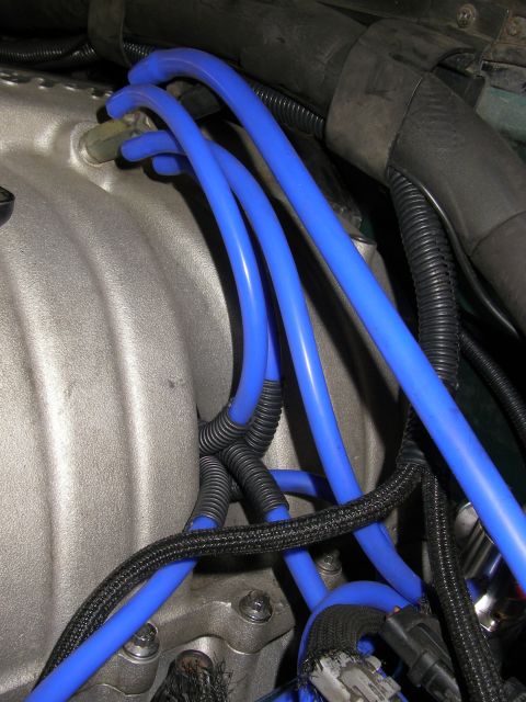1990 Ford Bronco - Close-up of an engine bay showing bright blue silicone spark plug wires routed across a cast-aluminum intake manifold, with black corrugate…