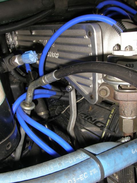 1990 Ford Bronco - Engine-bay detail of a finned aluminum valve cover with bright blue spark-plug or vacuum lines routed across it, plus rubber hoses labeled…