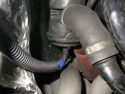 1990 Ford Bronco - Close-up down inside an engine bay showing a black vacuum line with a blue plastic connector routed through corrugated split loom, tapping…