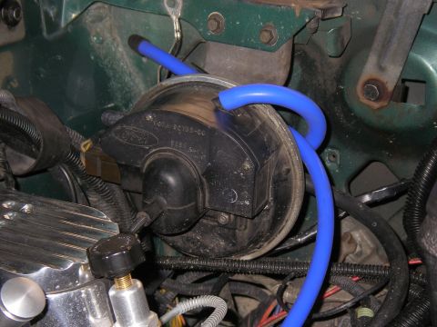 1990 Ford Bronco - Detail shot inside a green engine bay of a black Ford-branded vacuum canister/actuator stamped part number E0TA-9C735-CC, with a bright blu…