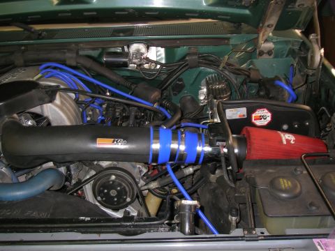 1990 Ford Bronco - Overhead view into a green truck's engine bay fitted with a K&N cold air intake, black tube with blue silicone couplers feeding a red conic…