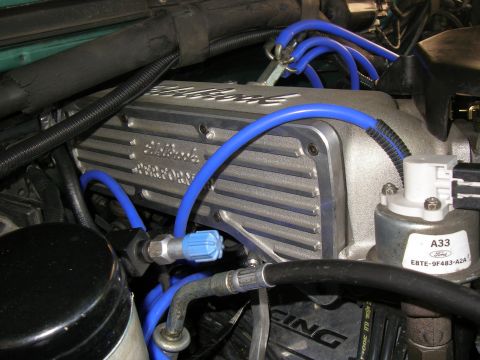 1990 Ford Bronco - Engine bay close-up of a finned cast-aluminum Edelbrock Performer intake manifold upper plenum, with blue silicone plug wires and blue vacu…