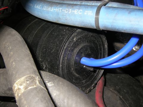 1990 Ford Bronco - Dusty engine-bay close-up of a black plastic vacuum reservoir canister with a blue silicone vacuum line plugged into its nipple. A blue coo…