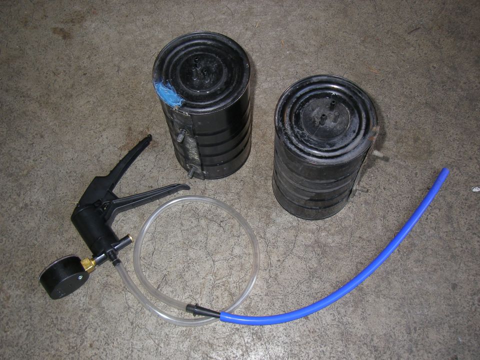 Vacuum pump with gauge, clear tubing, and two black canisters with blue tape on one