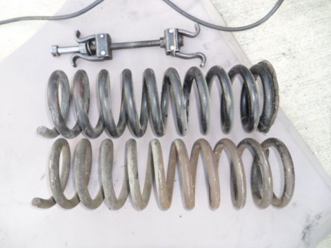 1973 Ford Ranchero - A spring compressor tool sits above two sets of used coil springs, one set appearing darker than the other.