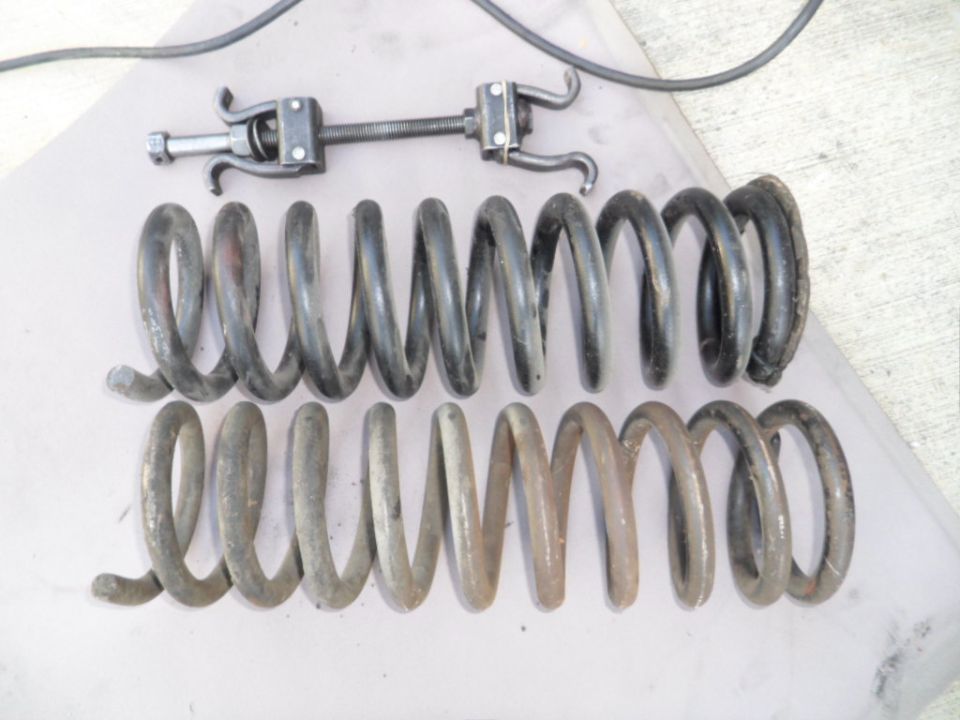 Two sets of coil springs and a spring compressor tool on a flat surface