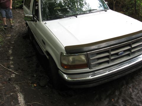 1994 Ford Bronco - A white Ford Bronco is stuck in the mud on a trail, with a person standing nearby.