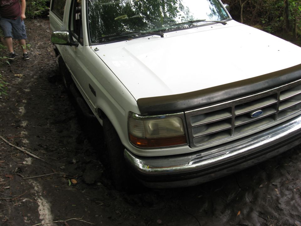 White Ford Bronco with a black bug deflector stuck in mud, front grille and headlights visible