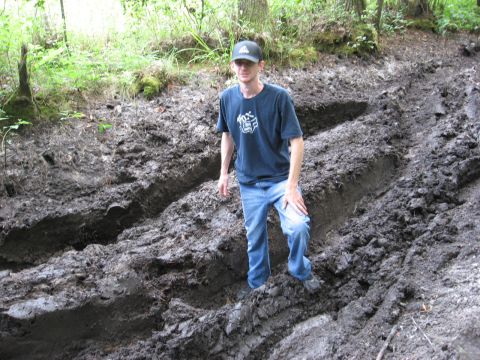 1994 Ford Bronco - A man stands in deep mud tracks within a wooded area, suggesting off-road activity.
