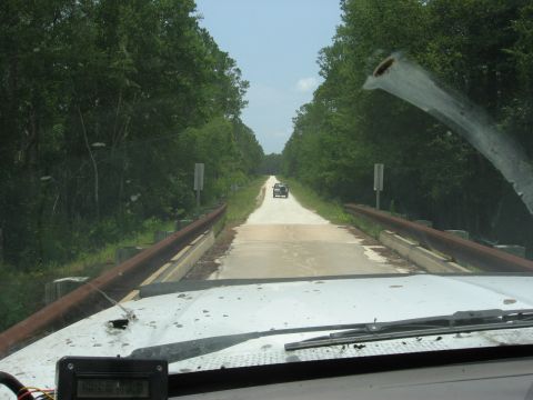 1994 Ford Bronco - Two vehicles drive on a narrow bridge surrounded by trees.