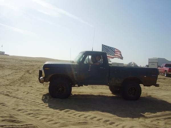 Lifted Ford pickup with American flag driving on sand dunes