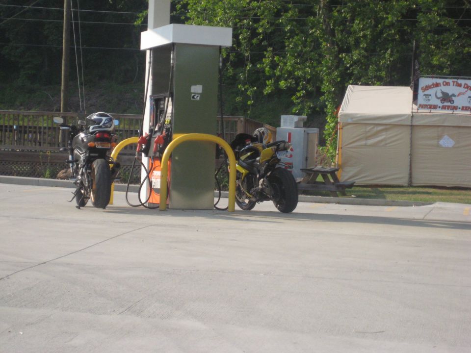 Two sport motorcycles parked at a gas pump, one black and one yellow
