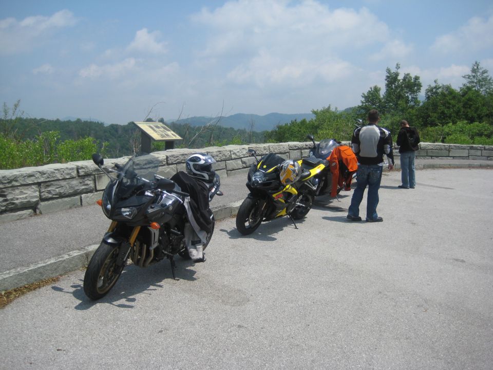 Three motorcycles parked on asphalt with a stone wall and scenic overlook