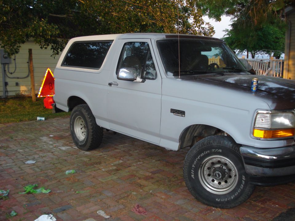 Ford Bronco parked on brick driveway, primer gray paint, some rust on hood