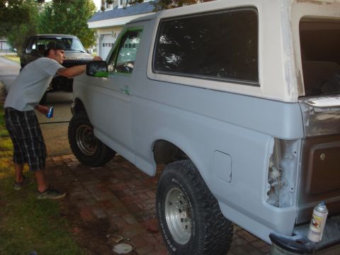 1993 Ford Bronco - A person works on a gray Ford Bronco with a white top, with another dark SUV parked behind it.