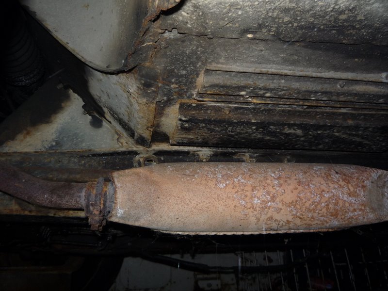 Underside of a vehicle showing a rusted exhaust pipe and heavily corroded frame components