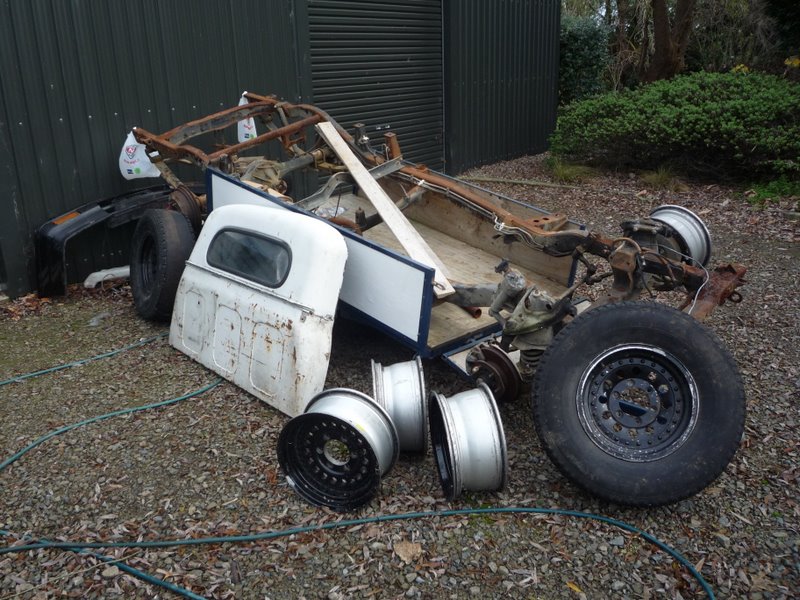 Disassembled vehicle chassis, white body panel, and wheels on gravel