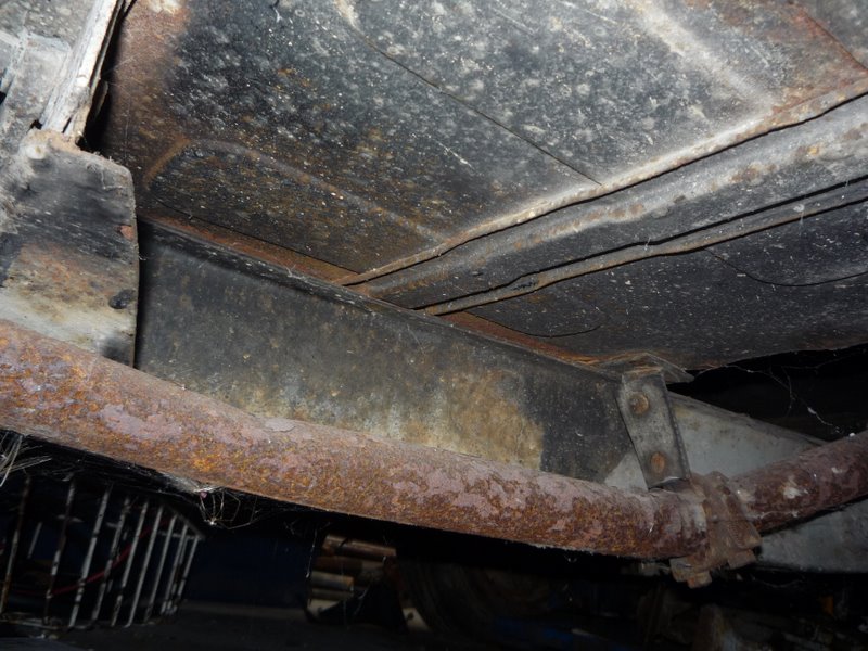 Underside view of a vehicle showing a rusted exhaust pipe, frame rails, and underbody